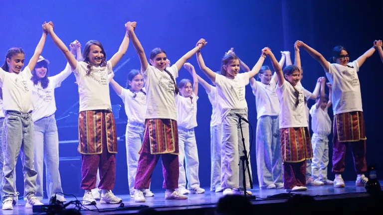 Jongeren in witte T-shirts staan hand in hand met opgeheven armen op een podium in blauw licht