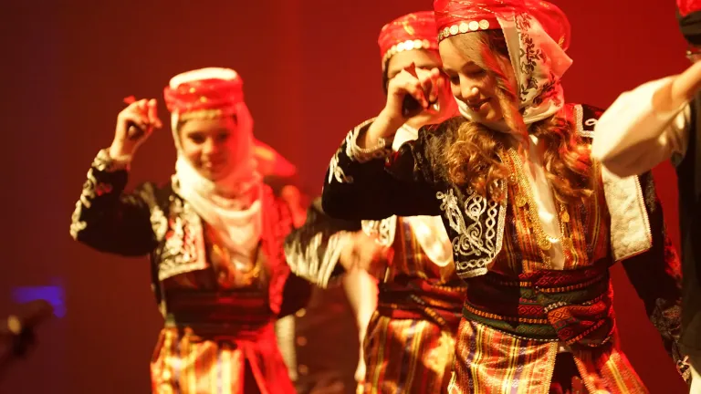 Dansers in traditionele klederdracht met hoofddoeken dansen in rood licht