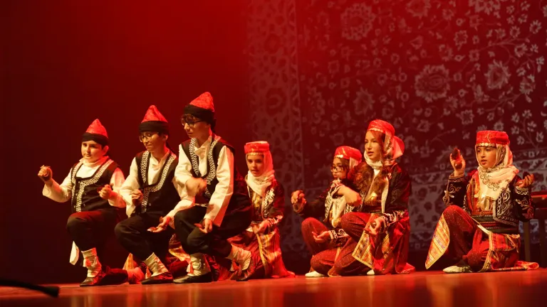 Een groep in traditionele klederdracht danst gehurkt op het podium