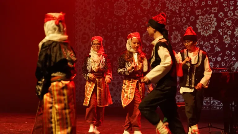 Een dansgroep in traditionele klederdracht met rode hoeden voert een folkloredans uit