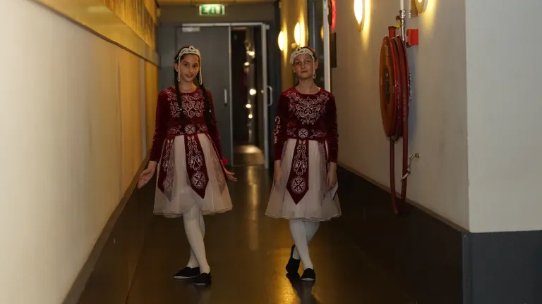Twee meisjes in rode klederdracht lopen door de gang achter de schermen