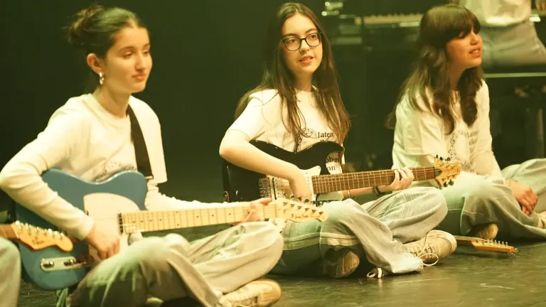 Drie meisjes zitten met elektrische gitaren op het podium