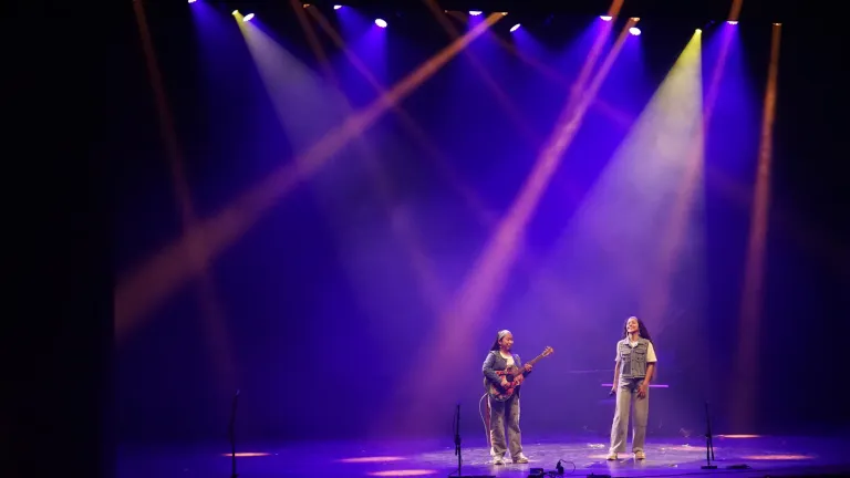 Twee jonge muzikanten staan met gitaren op het podium onder paarse lichtbundels