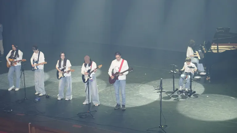 Jonge gitaristen staan op een rij op het podium onder lichtspots