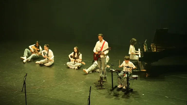 Een jonge band met gitaren, piano en drums speelt op het podium in groen licht