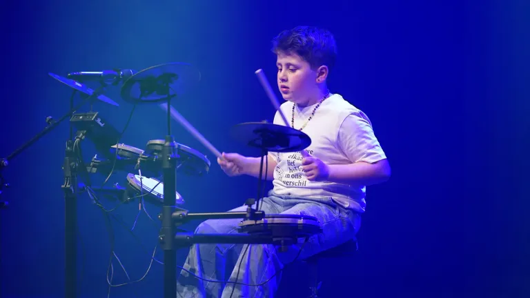 Een jongen in een wit T-shirt speelt drums op het podium
