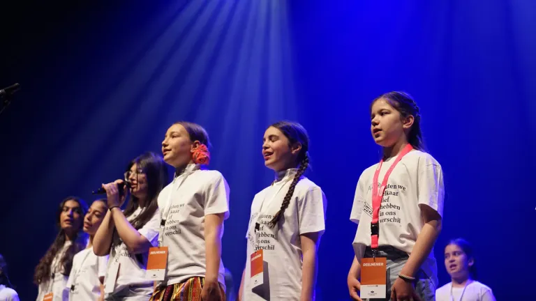 Een groep meisjes zingt samen in microfoons op het podium in blauw licht