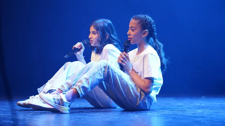 Twee meisjes zitten op het podium en zingen samen in blauw licht