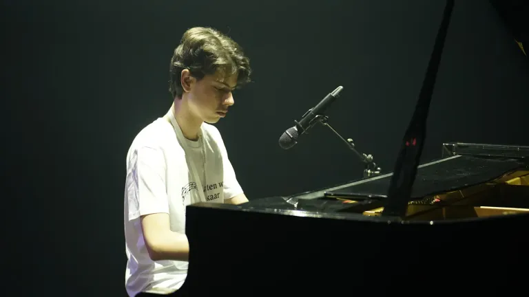 Een jongen speelt piano op een donker podium