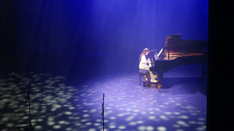 Een pianist speelt alleen aan de vleugel op een podium vol blauw licht