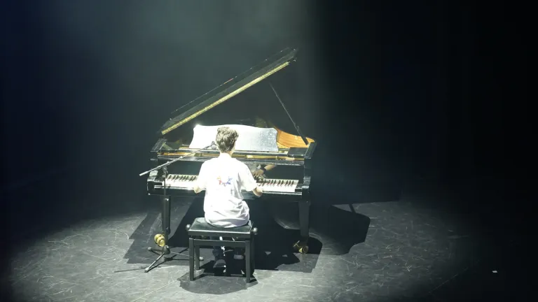 Een jonge pianist speelt aan de vleugel in een felle lichtbundel op een donker podium