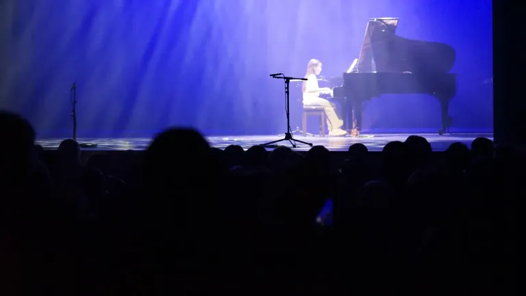 Een pianist speelt op een podium in blauw licht, met het publiek als silhouet op de voorgrond