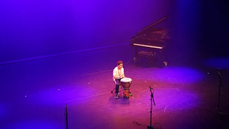 Een jongen speelt op een trommel op het podium in paars licht