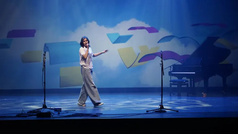 Een meisje zingt op het podium voor een blauw decor met een vleugel