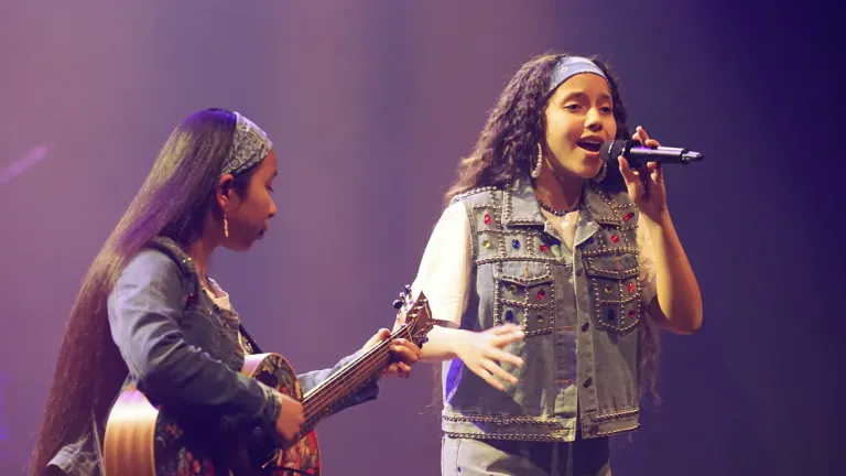 Een meisje zingt in de microfoon terwijl een ander meisje gitaar speelt