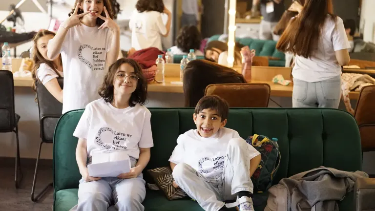 Twee kinderen in witte festival-T-shirts zitten ontspannen op een groene bank