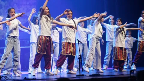 Een grote groep jongeren in witte T-shirts danst met uitgestrekte armen op het podium