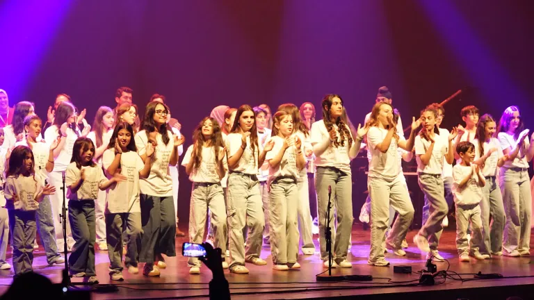 Een grote groep jongeren danst op het podium in paars licht