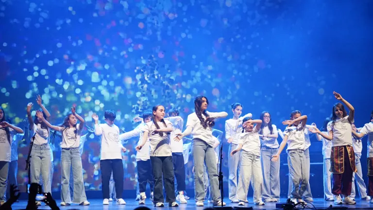 Jongeren dansen in een lange rij voor een decor met kleurrijke lichtpuntjes