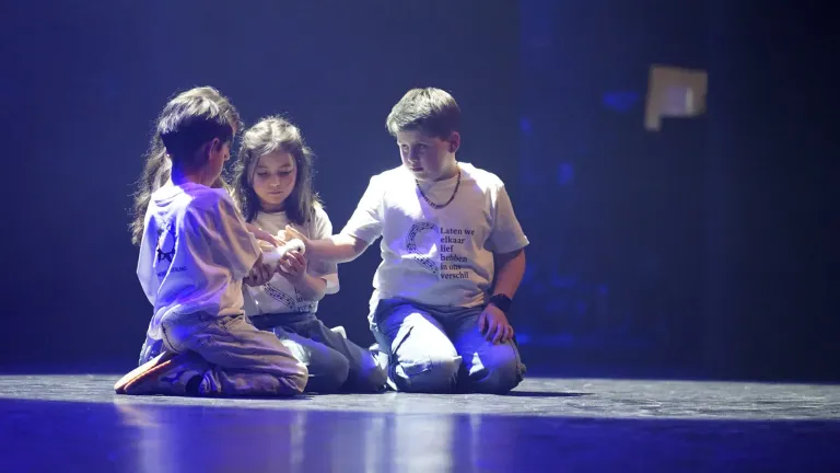 Drie kinderen knielen samen op het podium tijdens een scène