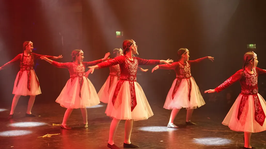 Meisjes in rode fluwelen jurken met witte tule rokken dansen in rood podiumlicht