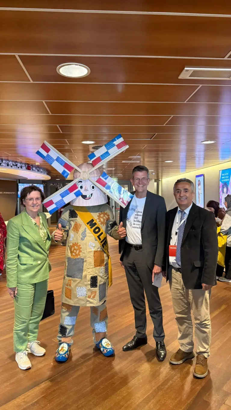 De molenmascotte Molie poseert met twee gasten in een zaal met houten plafond